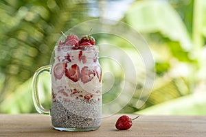 Almond milk chia pudding with fresh red strawberries, goji berries and oat flakes in a glass jar mug. Vegan raw breakfast. Chia