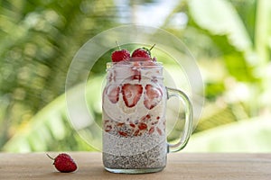 Almond milk chia pudding with fresh red strawberries, goji berries and oat flakes in a glass jar mug. Vegan raw breakfast. Chia