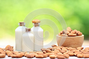 Almond milk in glass bottle with almonds in a bowl on the table blurred natural green background