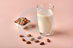 Almond milk in glass and nut seeds on pink powder background
