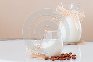 Almond milk in a glass and a pitcher with almond seeds on marb