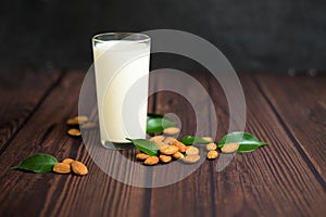 Almond milk in a glass on a wooden background. close-up of almond seeds and green leaves next to the glass. space for