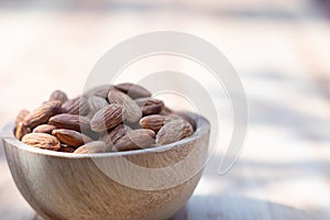 Almond nut in wooden bowl on wood table with green leaf background, copy space