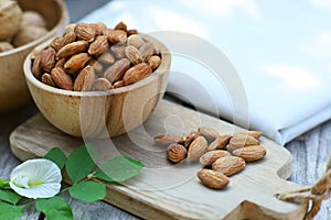 Almond nut in wooden bowl on wood table with green leaf background, copy space