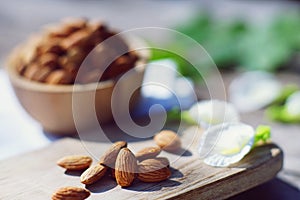 Almond nut in wooden bowl on wood table with green leaf background, copy space