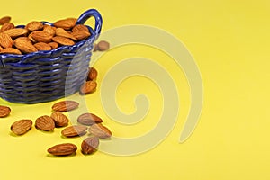 Almond nuts in a blue glass basket and on a yellow surface