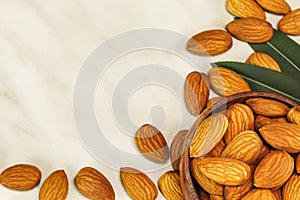Almond nuts lie in a brown wooden bowl and on white marble