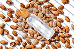 Almond nuts scattered white wooden table, bottles of culinary and cosmetic skincare seed oil