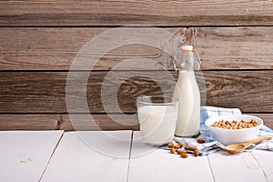 Almond or soy milk in bottle and glass, bowl with almonds scattered around on rustic wooden background. Cow milk alternatives