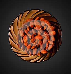Almonds on a glass brown plate. Isolated on black background. Top view