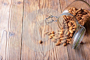 Almonds in a glass jar scattered on an old wooden table in cracks. Photo, image/