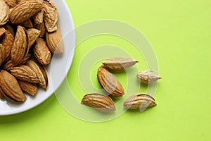 Almonds are not peeled on white plate. Yellow background. View from above. Roasted almonds for a snack. Nuts. Food. Quenching