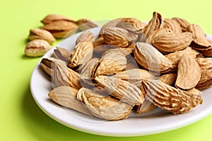 Almonds are not peeled on a white plate. Yellow background. View from above. Roasted almonds for a snack. Nuts. Food. Quenching