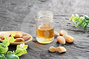 Almonds oil in clear glass bottles and pile of roasted almonds in brown wooden spoon placed on black wooden plank,