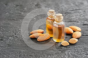 Almonds oil in clear glass containers and pile of roasted almonds on black wooden board.