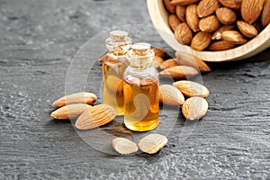 Almonds oil in glass containers and heap of roasted almonds on black wooden plank.