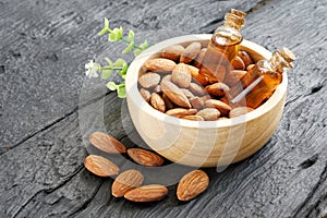 Almonds oil in wooden bowl with roasted almonds on black wooden plank