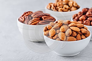 Almonds, pecans, walnuts and hazelnuts in white bowls on grey background. Nuts mix. Healthy food and snack.