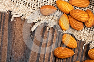 Almonds are scattered on a wooden table covered with a homespun cloth with a rough texture