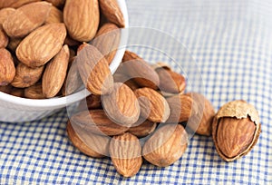 Almonds in a white ceramic bowl on the blue cloth background.