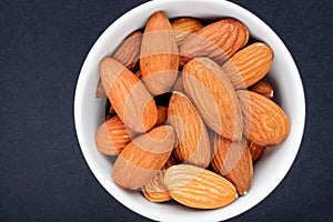 almonds on white plate close up on black slate background top view