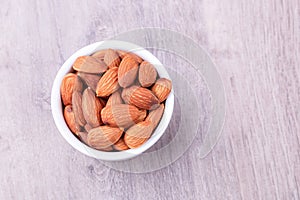 Almonds in white porcelain bowl on wooden table. Almond concept with copy space