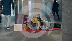 An almsman is lying in the underpass with his dog near him