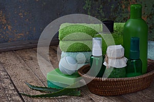 Aloe composition of beauty threatment products in green colors on brown wooden background: shampoo, soap, bath salt, towel, oil. V