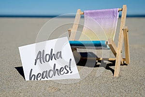 ALOHA BEACHES text on paper greeting card on background of beach chair lounge summer vacation decor. Sandy beach sun