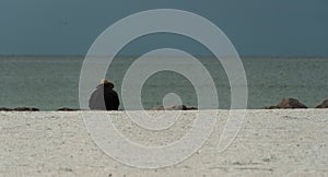 Alone beachgoer in straw hat and black jacket watching horizon line