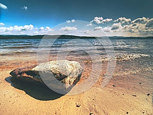 Alone big stone in water close to the beach. Stormy sky above