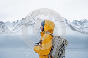 Alone brave woman traveler with backpack looking away to winter mountains