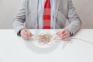 Alone businessman try to unwinds tangled thread ball like puzzle out situation. Conceptual photo