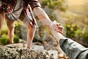 Alone we climb rocks, together we climb mountains. Cropped shot of hikers helping each other climb up a rock in nature.