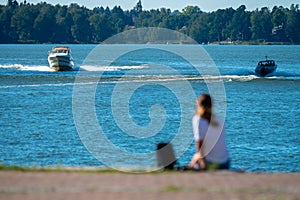 An alone female sitting on the waterfront watching the sea and passing by leisure boats