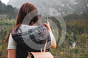 Alone female tourist in vesta and backpack taking a photo on the smartphone of amazing mountain range in High Tatra