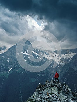 Alone hiker man in red jacket against the gloomy mountain top landscape with thunder cloudy sky