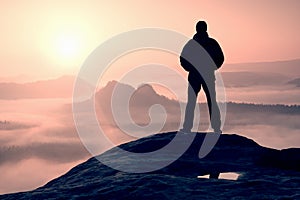 Alone hiker standing on top of a mountain and enjoying sunrise
