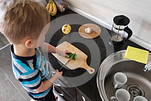 Alone independence vegetarian child cuts green cucumber with knife in kitchen, vegan kid montessori training, side view