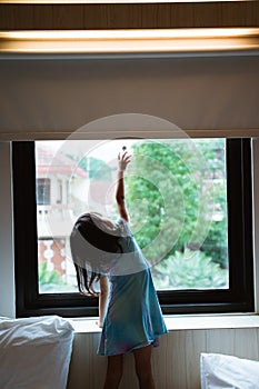 Alone little girl reaching window curtain