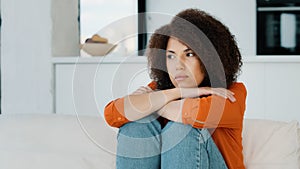 Alone lonely stressed African American woman sitting with sad problem at home couch thinking about trouble looking away