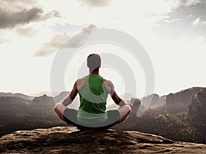 Alone man is doing Yoga pose on the rocks peak within misty morning. Middle-aged man practicing yoga