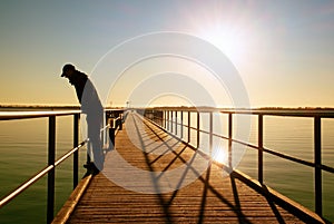 Alone man on pier and look over handrail into water. Sunny clear sky, smooth water