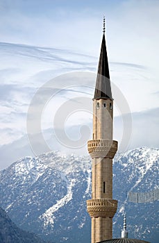 Alone minaret rise against the backdrop of impregnable snow-capped mountains covered with trees under serene blue sky