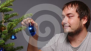 Alone positive european man hangs a ball on the Christmas tree. Concept of expectation of miracle magical holiday