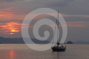 Alone sailboat at sunset. Atmospheric seascape with orange sun.