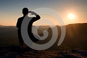 Alone sportsman in black. Tall hiker in squatting position enjoy view at sunset on mountain peak