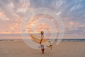 Alone surfer woman on beach with warm sunset tones. Attractive surfgirl with surfboard