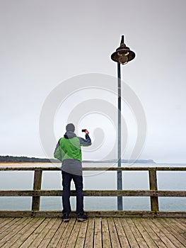 Alone tourist guide at sea pier handrail, autumn misty morning.Man stay bellow old lamp.