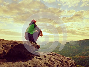 Alone tourist take a rest. Hiker in green black jacket sitting on the rocky peak